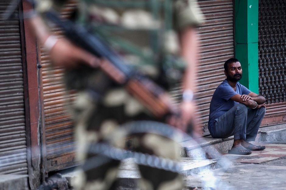 A security personnel stands guard as a man sits in front of a closed shop in Jammu on August 6, 2019. (Photo: Rakesh BAKSHI / AFP)
