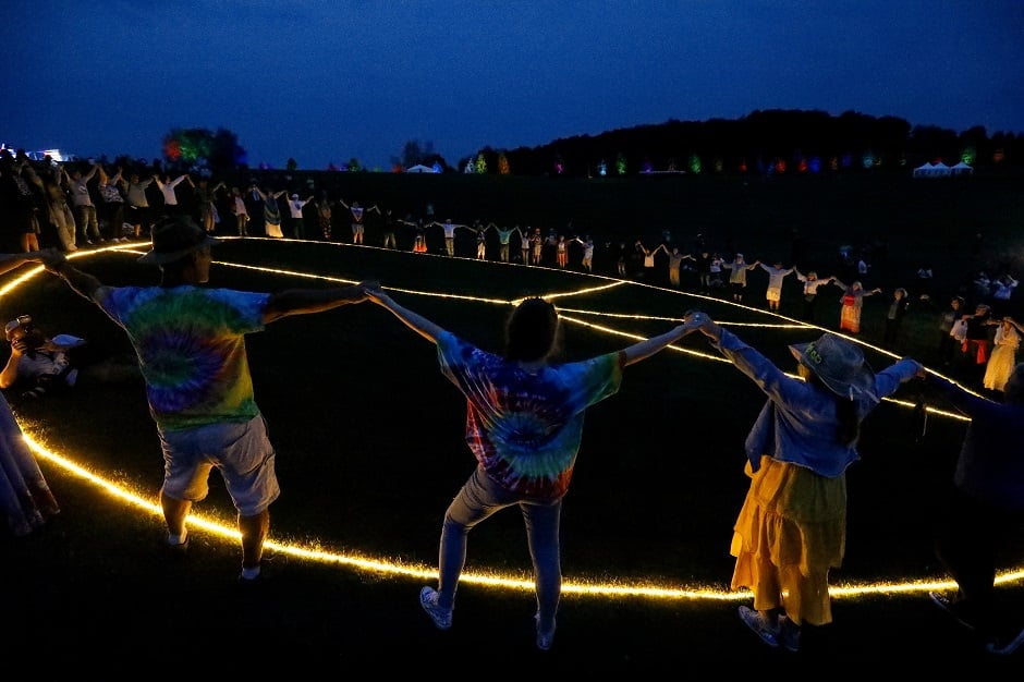 People hold hands in a circle around a large, illuminated peace sign on a field at the original site of The Woodstock Festival for Arts, in Bethel, New York, US. Photo: REUTERS