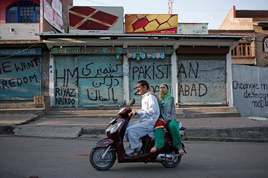 Kashmiris ride on a scooter past the closed shops painted with graffiti during restrictions, after scrapping of the special constitutional status for Kashmir by the Indian government, in Srinagar. PHOTO: REUTERS