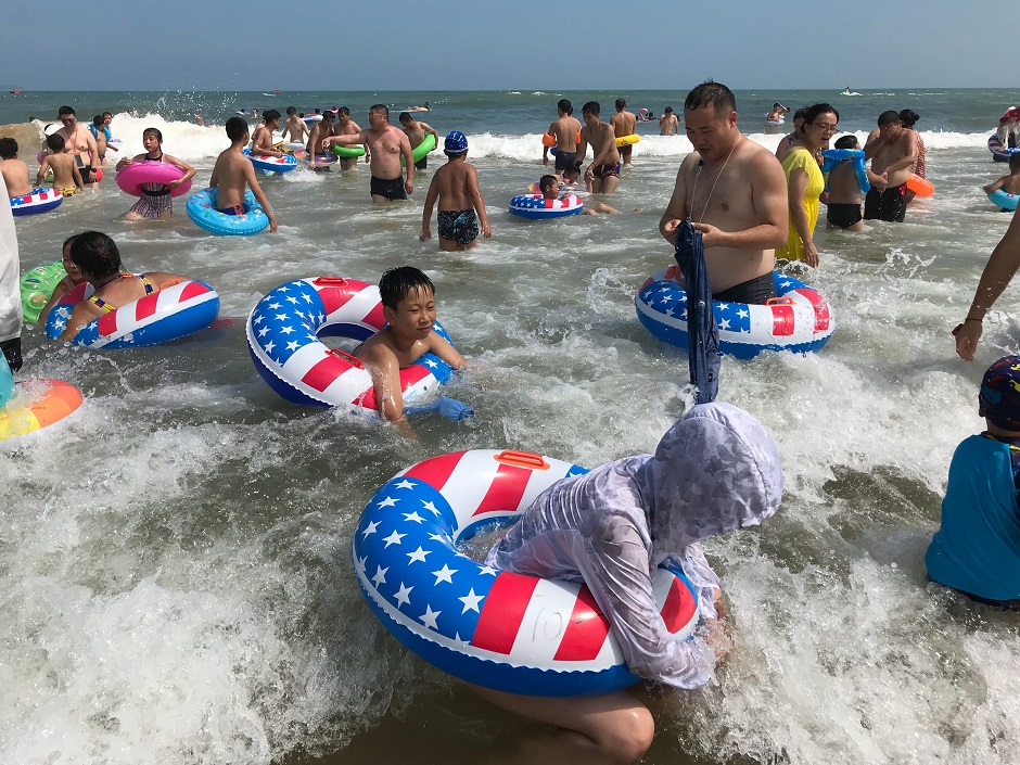 Beachgoers with rubber rings, adorned with the colours of the US national flag, cool themselves by a beach in Qingdao, eastern China's Shandong province. PHOTO: AFP
