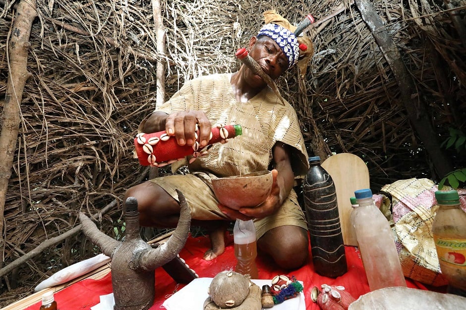 Chief Baykuh, a traditional healer in his shrine at Magbumoh village mixes herbs into potions. In his mouth he holds an animal horn called a ke'elen which is used to communicate with the gods who guide him. PHOTO: AFP