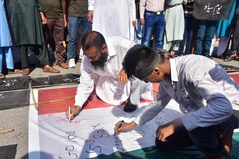 Activists of Hizbul Mujahideen (HM), a Kashmiri separatist group, write comments on an Indian flag during a protest in Muzaffarabad, the capital of Pakistan-controlled Kashmir, as the country observes 'Black Dayâ. PHOTO: AFP