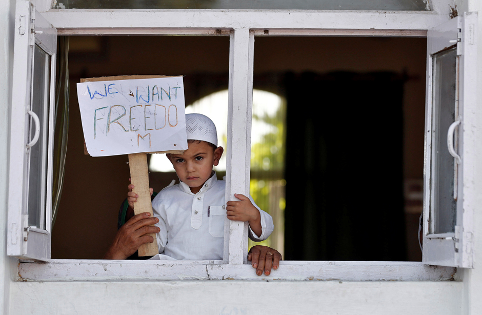 A Kashmiri boy displays a placard from a window at a protest site after Friday prayers during restrictions in Srinagar on August 23, 2019.