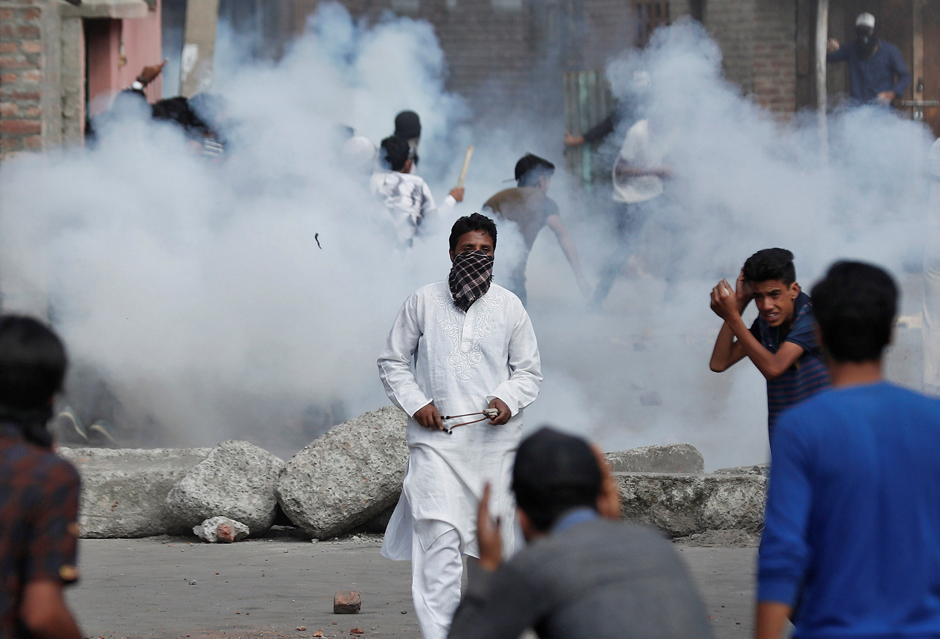 Kashmiris run for cover as smoke rises from teargas shells fired by Indian security forces during clashes in Srinagar on August 23, 2019.