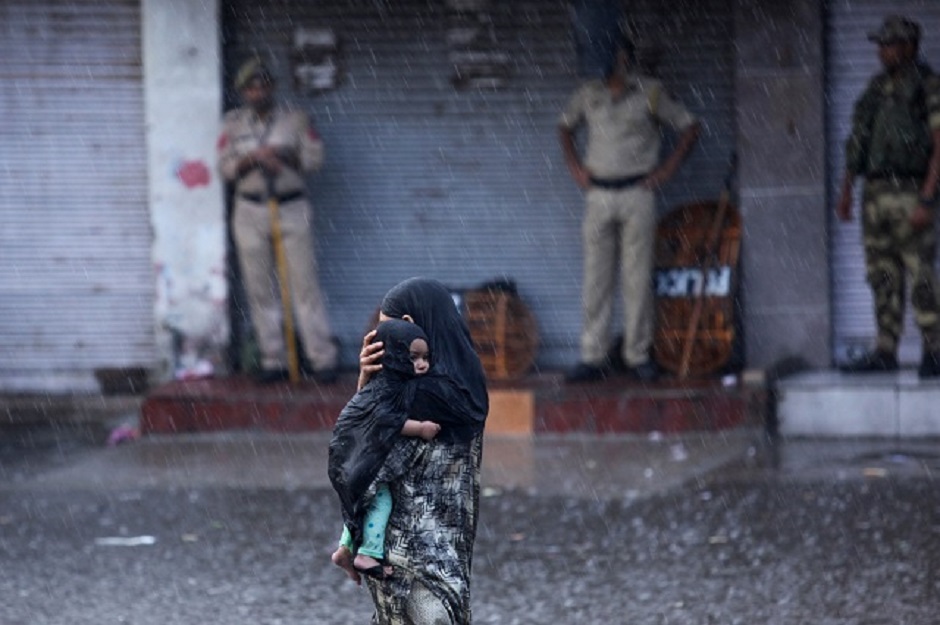 A woman holds her child as she walks past security personnel under rain in Jammu on August 5, 2019 - Authorities in Indian-administered Kashmir placed large parts of the disputed region under lockdown early August 5. (Photo by Rakesh BAKSHI / AFP)