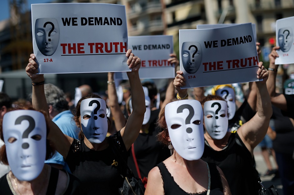 People with masks bearing a question mark hold a placard reading 