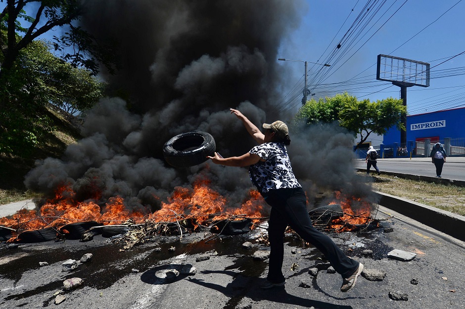 A woman throws a tire to a bonfire during a roadblock by students and health workers protesting to demand the resignation of Honduran President Juan Orlando Hernandez for his alleged links with drug trafficking. PHOTO: AFP