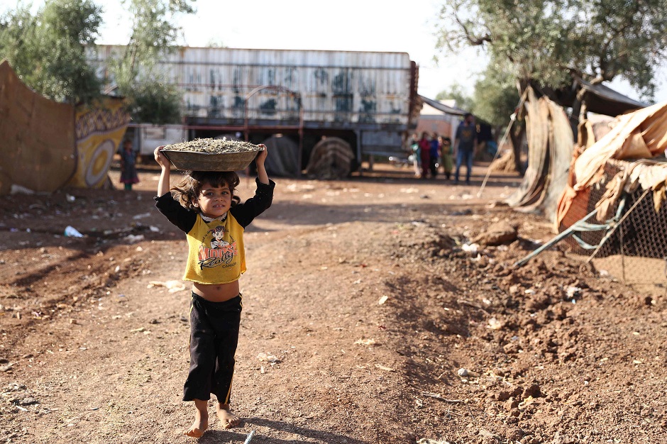 A child walks carrying a basin over the head on a footpath by a field at a camp for displaced Syrians near the village of Shamarin, near the border with Turkey in the northern Syrian Aleppo province. PHOTO: AFP