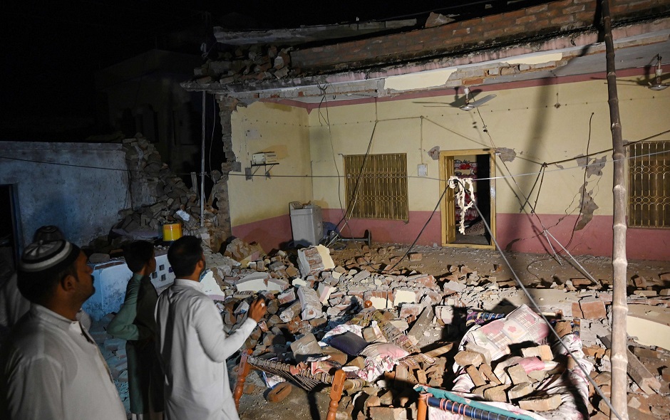 Pakistani men stand beside a collapsed building following an earthquake on the outskirts of Mirpur. PHOTO: AFP