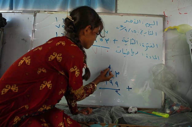 A displaced Syrian girl writes on a whiteboard inside the bus converted into a classroom (Photo: AFP)