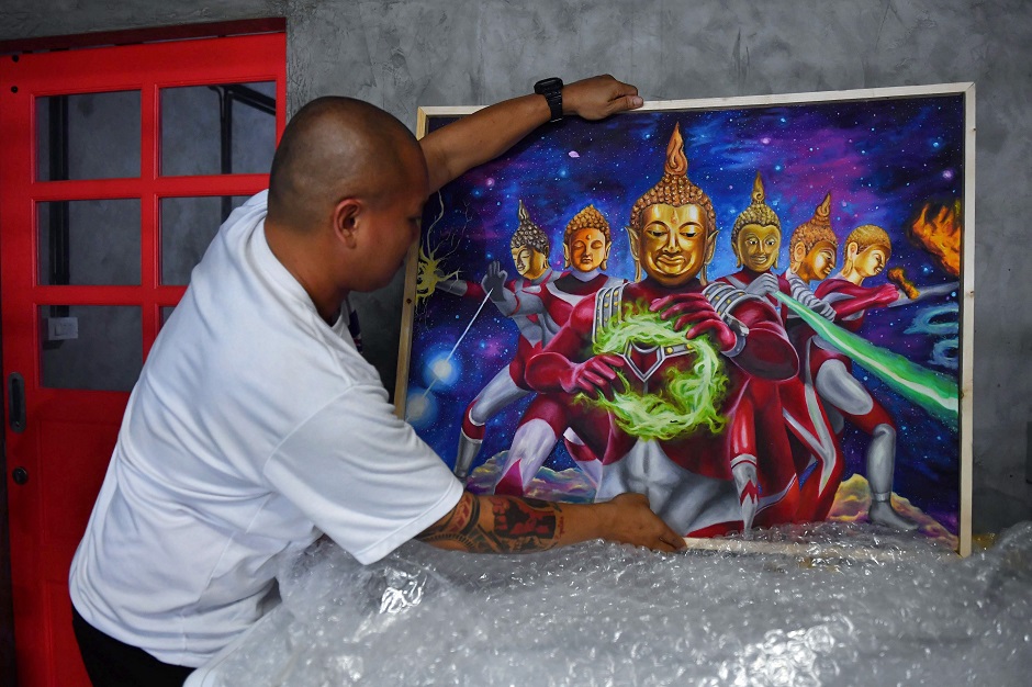 Collector Pakorn Porncheewangkul arranges a painting depicting Buddha as Japanese superhero Ultraman in his home in Bangkok. PHOTO: AFP