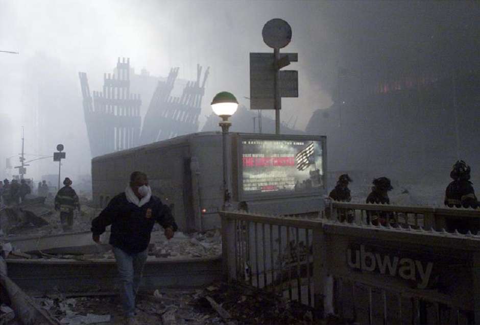 The wreck of the World Trade Center smolders in the background as a man passes a subway stop near the World Trade Center towers, September 11, 2001. PHOTO: Reuters