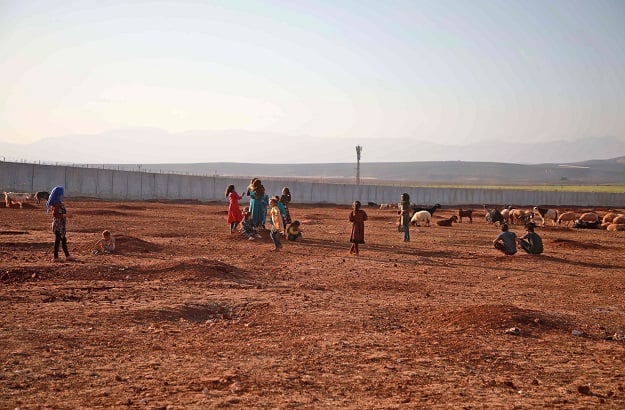 Children play in an open field near of the barbed-wire-topped concrete fence demarcating the border between Syria and Turkey, at a camp for displaced Syrians in Atme. (Photo: AFP)