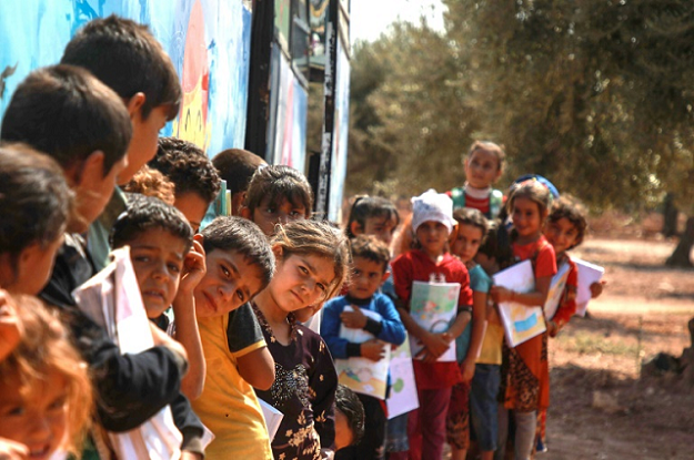 Displaced Syrian children queue for their turn outside a bus converted into a classroom in Idlib in September 2019. PHOTO: AFP