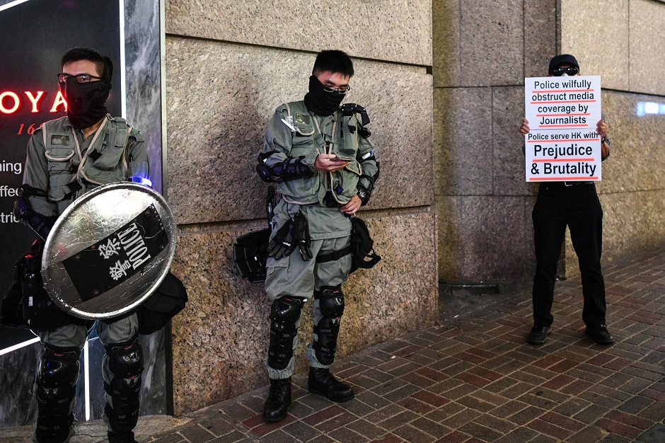 A man holds a protest poster next to policemen in the Lan Kwai Fong area as people celebrate Halloween. PHOTO: AFP