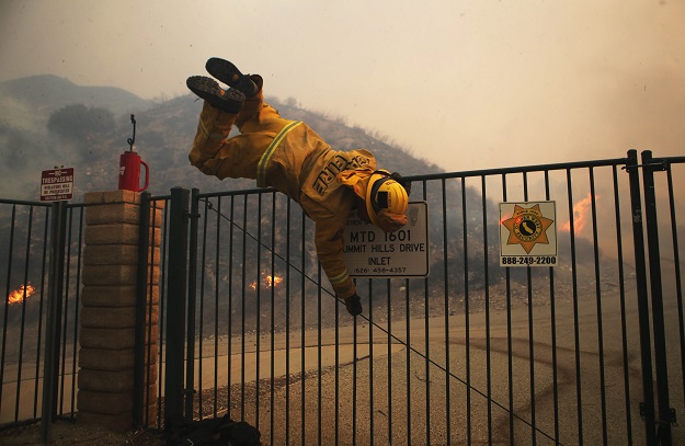 A Cal Fire firefighter hops over a locked gate while working the Tick Fire. PHOTO: AFP
