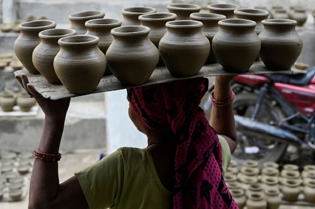 A woman carries clay pots for drying on an open space. PHOTO: AFP