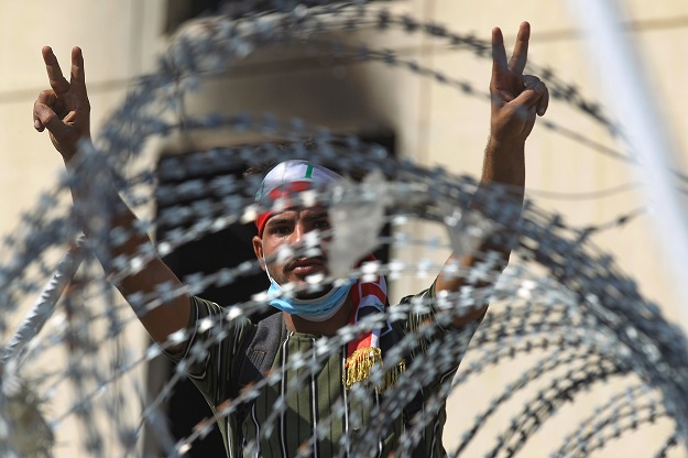 An Iraqi protester flashes the victory sign from behind barbed wire near the capital Baghdad's Al-Jumhuriyah Bridge (Photo: AFP)