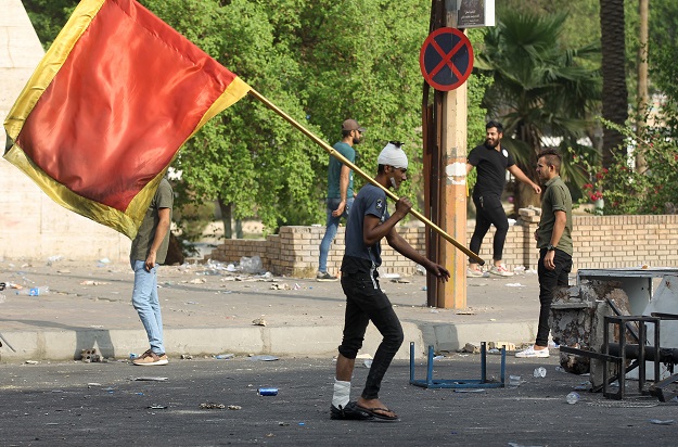 A man who was injured during prior protests walks holding a red banner during clashes with riot police amidst demonstrations (Photo: AFP)