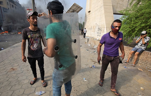 A protester holding a riot police plastic shield sprays fizzy cola drink from a bottle onto the face of another protester to relieve the effects of tear gas during clashes with riot police amidst demonstrations (Photo: AFP)