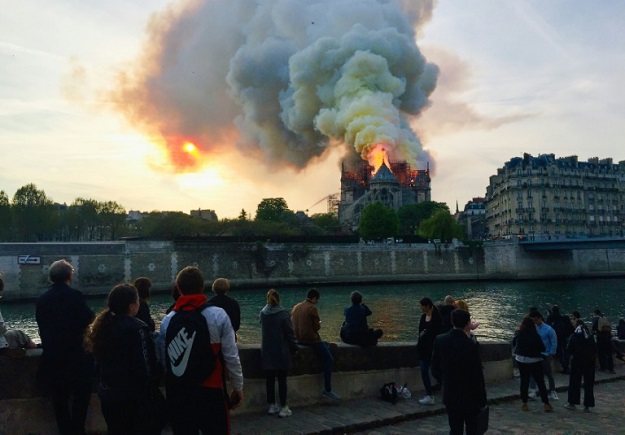 Bystanders look on as flames and smoke billow from the roof of Notre-Dame (Photo: AFP)