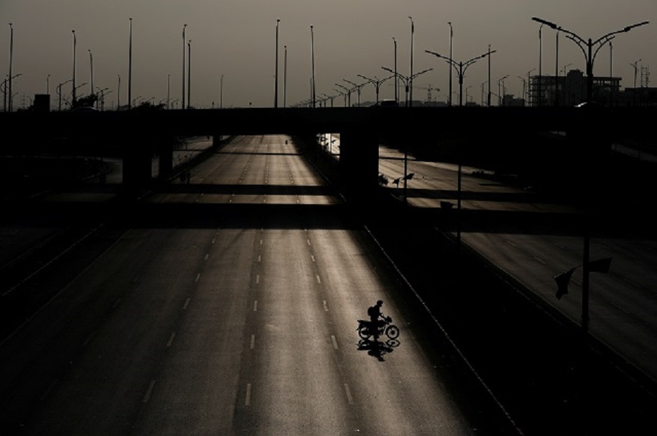 A man walks with his motorbike on a deserted road, blocked by shipping containers (unseen) leading towards the venue of Azadi March. PHOTO: REUTERS
