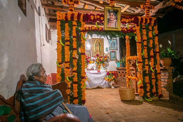 An elderly woman sits near offerings for the celebration of the Day of the Dead (Photo: AFP)