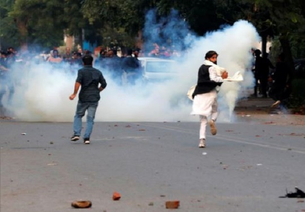 Demonstrators run for cover as smoke billows from a tear gas shell fired during a protest against a new citizenship law, in New Delhi, India. PHOTO: REUTERS