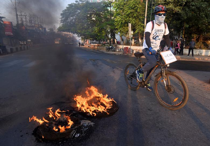 A cyclist with an anti-Citizenship Amendment Bill (CAB) placard hanging on his bicycle passes burning tyres set ablaze by protesters during a strike called by All Assam Chutia Students' Union (AACSU) to protest against the bill. PHOTO: Reuters