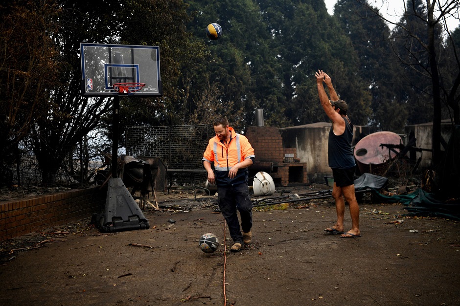 Cobargo resident John Aish and Nathan (L) shoot some hoops in the still standing hoop outside their destroyed homes in Cobargo, Australia January 6, 2020. PHOTO: REUTERS