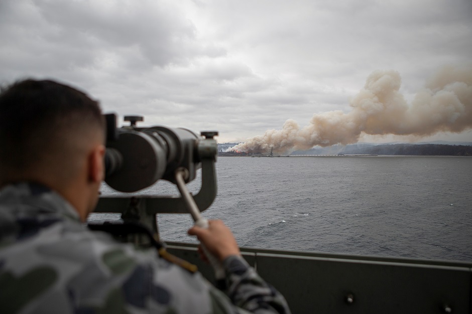 Seaman Boatswains Mate Malik El-Leissy views a burning fire from HMAS Adelaide as the ship arrives at Eden, NSW, Australia, during Operation Bushfire Assist 2020. PHOTO: REUTERS