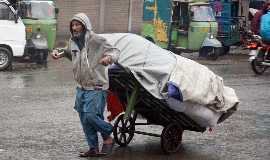 A labor carries a loaded wheelbarrow during a rain spell in Lahore. PHOTO: ONLINE