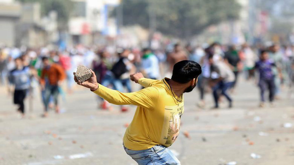 A man supporting a new citizenship law throws a stone at those who are opposing the law, during a clash in New Delhi, February 24. PHOTO: REUTERS