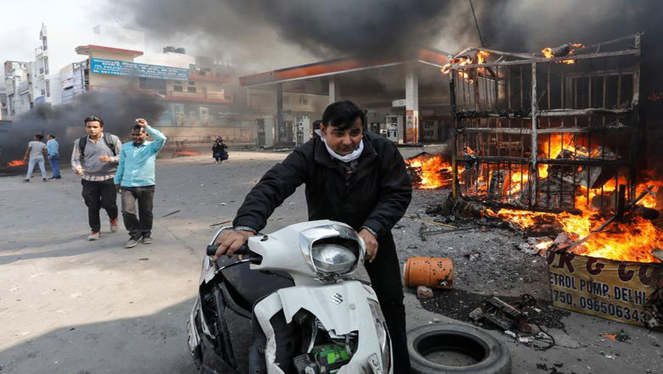 A man pushes his damaged scooter past a burning petrol pump during a clash between people supporting a new citizenship law and those opposing it, in New Delhi, February 24. PHOTO: REUTERS