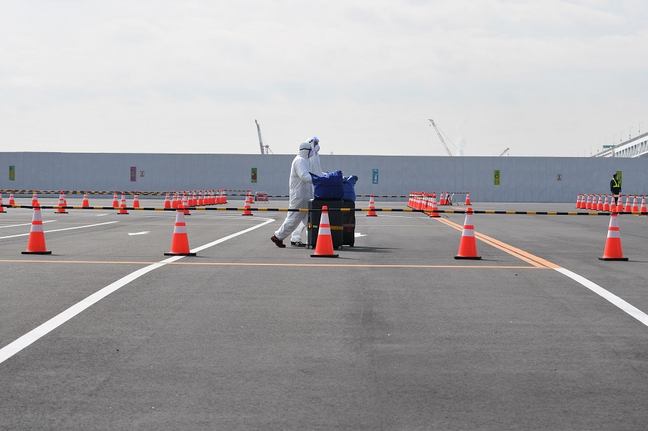 Workers in protective suits help passengers with their luggages from the Diamond Princess Cruise ship, in quarantine due to fears of new COVID-19 coronavirus, at Daikoku pier cruise terminal in Yokohama. PHOTO: AFP