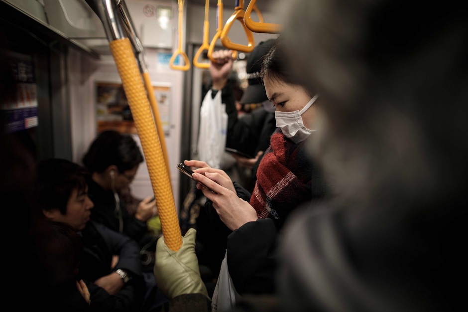 A woman wearing a facemask plays a video game on her smartphone on a subway train in Tokyo. PHOTO: AFP