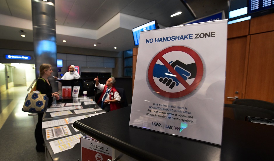 3 A traveller has questions answered at an information booth beside a reminder not to shake hands over Coronavirus concerns at Los Angeles International Airport on March 12, 2020 one day before a US flight travel ban hits 26 European countries amid ongoing precautions over the Coronavirus. PHOTO: AFP