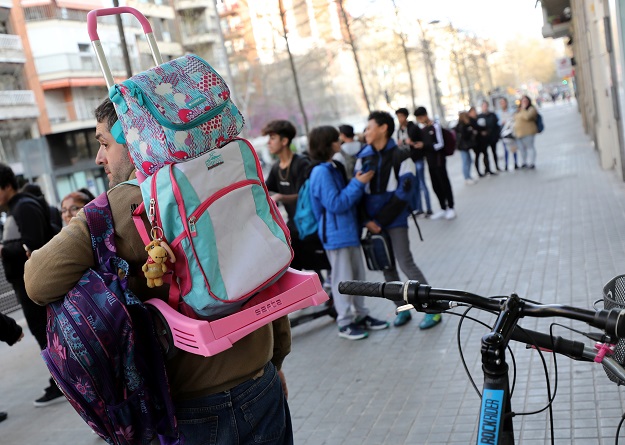 A father carries the backpack of his daughter as he waits for her at entrance of a school after Catalonia announced to close schools, kindergartens, institutes and universities from tomorrow as a precaution against coronavirus in Barcelona, Spain. PHOTO: Reuters