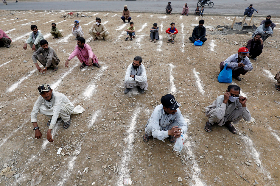 Men sit on the ground with lines drawn with chalk to maintain safe distance as they wait to receive sacks of ration handouts from a distribution point of a charity welfare during a partial lockdown in Karachi. PHOTO: Reuters